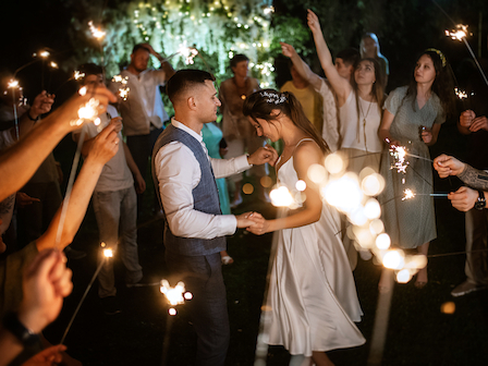 A couple is dancing surrounded by people holding sparklers at an outdoor night event, possibly a celebration or wedding.