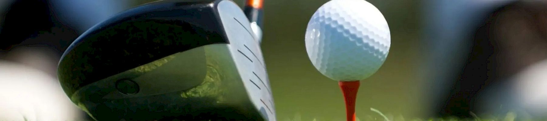 A close-up of a golf club poised to hit a golf ball on a tee on a golf course, with blurred background and green grass.