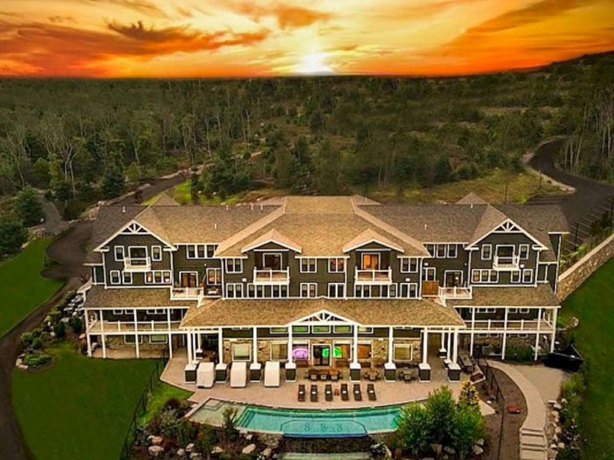 A large, elegant building with multiple balconies, a pool in front, surrounded by greenery, and a beautiful sunset in the background ends the sentence.