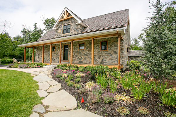 A stone house with a gable roof and a wooden porch, surrounded by a well-maintained garden and a stone path leading to the entrance.