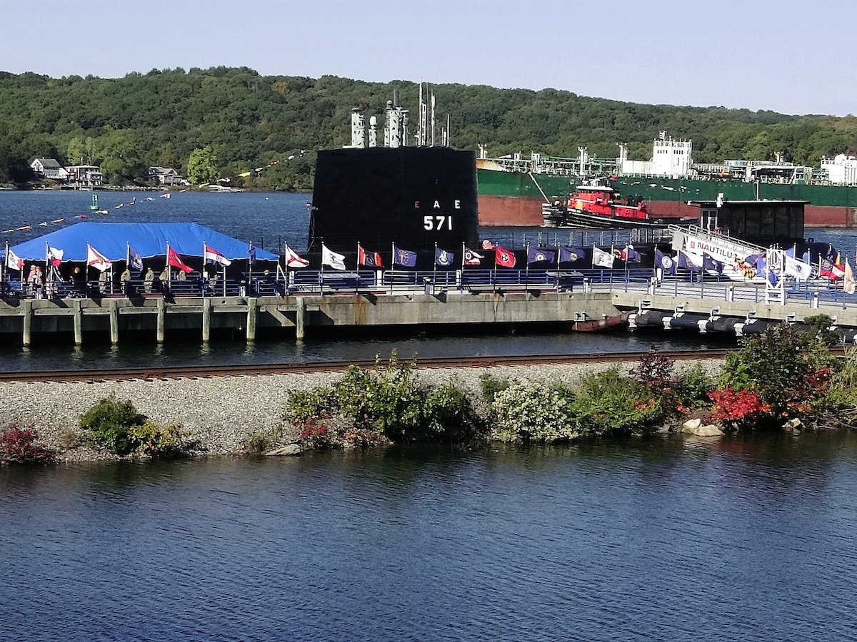 An outdoor setting features a dock with tents and flags, a large vessel labeled 