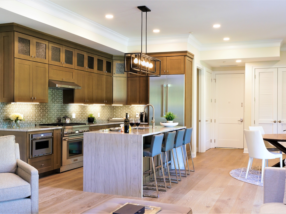 A modern kitchen and dining area with wooden cabinetry, a central island with blue stools, stainless steel appliances, and comfortable seating.