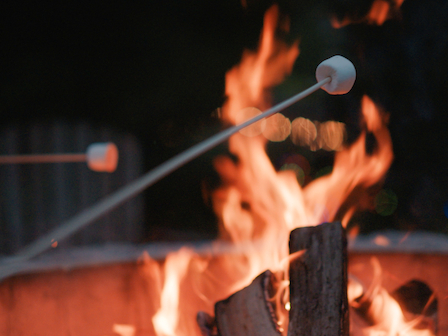 Two marshmallows being roasted over a campfire with flames in the background, creating a cozy and inviting atmosphere.