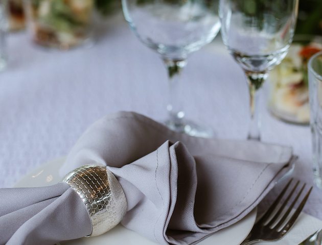 The image shows an elegant table setting with a white plate, silverware, a gray napkin in a holder, and two empty wine glasses.