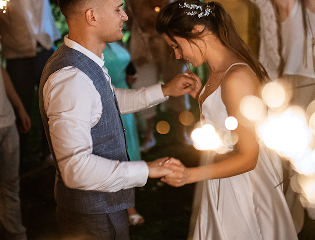 A couple is dancing at a festive event with sparklers in their hands, surrounded by people celebrating.