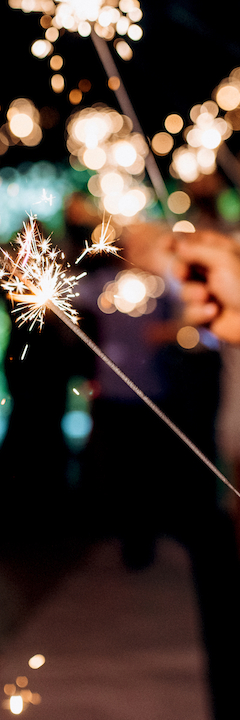 People holding sparklers in a festive or celebratory setting, creating a sparkling effect in the dark.