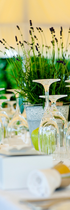 A formal table setting with upside-down wine glasses, a potted lavender plant centerpiece, and neatly arranged napkins and cutlery.